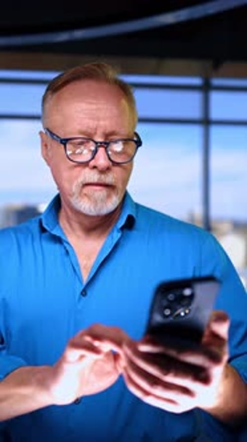 Focused adult male in blue shirt using his phone. Man is typing or setting an app on his smartphone.