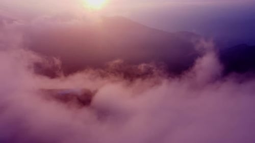 Aerial View Backwards Over the Morning Clouds with the Sun Rising Over the Mountains Golden Hour