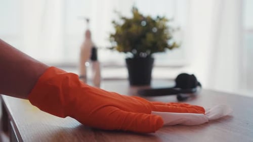Hand in Orange Glove wipes Wooden Table Surface