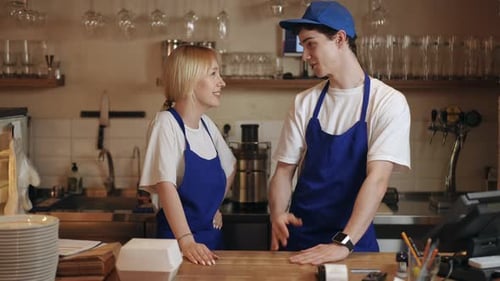 Two Cafe Workers Having a Nice Conversation and Laughing While Standing at Their Workplace Behind