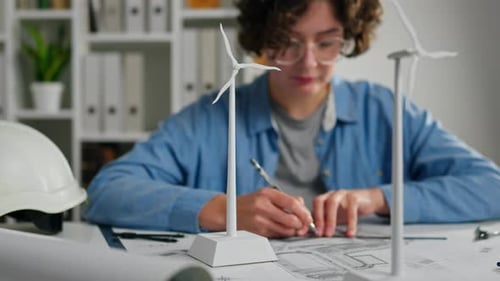 Young engineer designing renewable energy models with wind turbines at a workspace in the afternoon