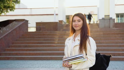 Cheerful Student Girl Hugging Books Posing with Backpack Near College Building Outdoor Smiling to