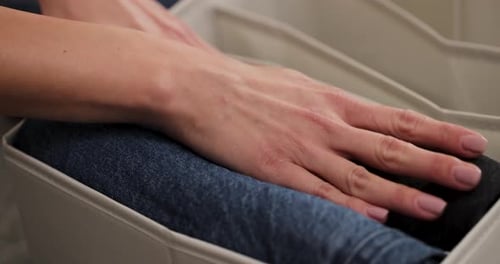 Un gros plan de la main d'une femme caucasienne avec des ongles peints ajustant un jean dans un organiseur de vêtements, c