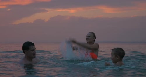 Family Splashing Water in Ocean at Sunset