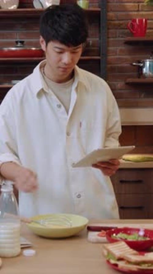 Young Adult Prepares Food in Kitchen With Tablet