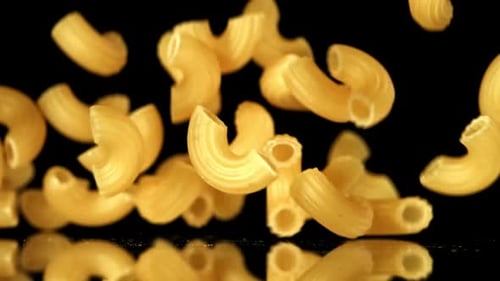 Elbow Macaroni Pasta Pieces Falling on Black Surface