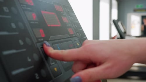Pulsa el botón de control con los dedos en una cinta de correr con uñas pulidas en el gimnasio