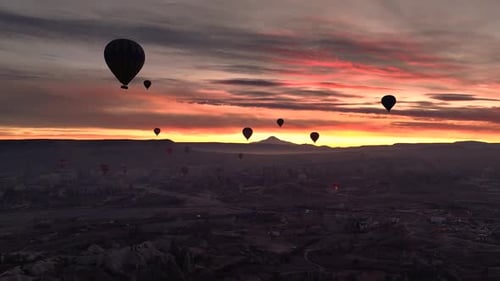 Drone view of dozens of balloons taking off at twilight, illuminated by burner flames in Rose Valley