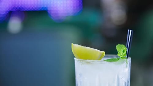 Upper part of glass filled with light beverage and two black straws in. Ice cubes,