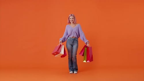 Woman with Shopping Bags Smiling in Orange Studio