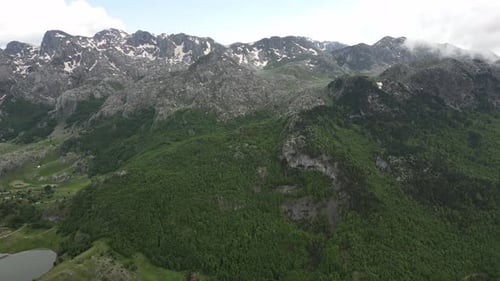 Flying over beautiful green mountains. In the background, stone cliffs with snow are visible.