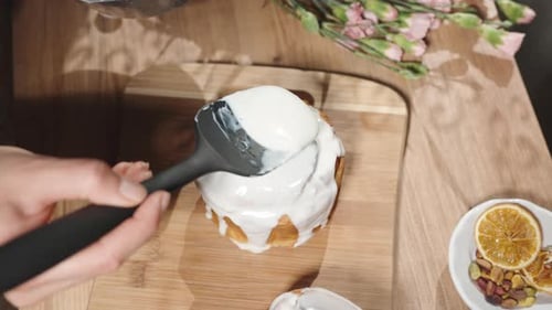 Top view: a woman covers a homemade Easter cake with white icing.