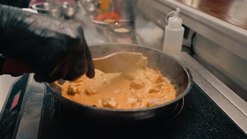 close-up of a chef in a professional restaurant kitchen adding sauce to a curry pan stirring dish