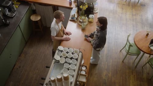 Top View of a Brunette Girl in a Gray Sweater Makes an Order at the Counter From the Barista of a