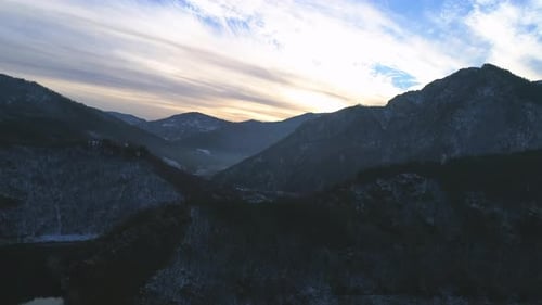 AERIAL: Flying above rocky mountains with a river between the basin at sunset