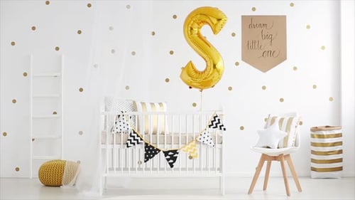 A newborns white wooden crib with golden balloon and pennants in bright nursery room