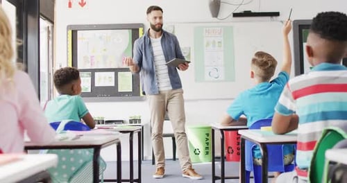 Diverse male teacher and happy schoolchildren at desk in school classroom