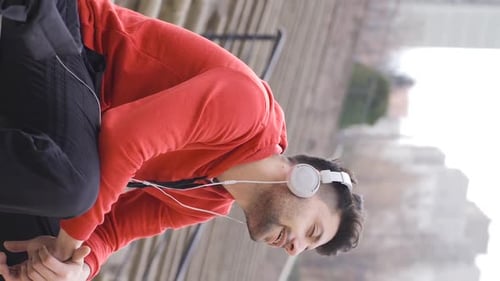 Vertical Video of Handsome man listening to music with headphones on bench outdoors.