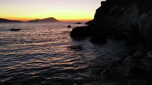 Sunset or sunrise slow forward flying with colorful and dramatic waves with rocky silhouette backdro