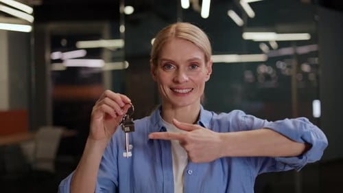 Real Estate Agent Pointing at Apartment Keys in Hand and Smiling at Office