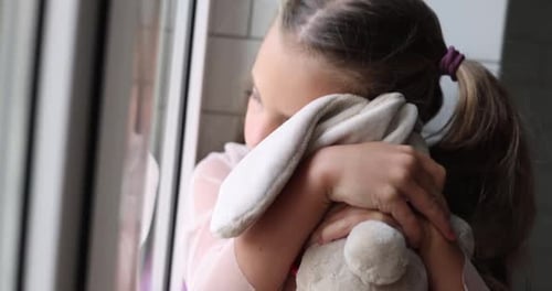 Child Hugging Toy Rabbit Standing by Window