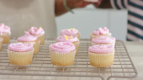 Los cupcakes se vuelven brillantes y salpican mientras el panadero inclina la coctelera para terminar la decoración en la rejilla para enfriar