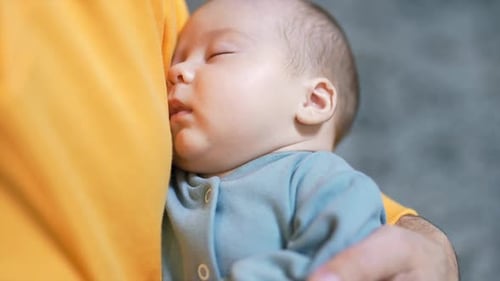 Newborn baby sleeping peacefully in daddy’s hands. Adorable sleeping child in a blue suit. Close up.