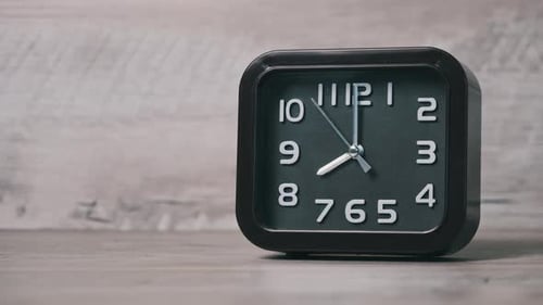 Eine quadratische Pfeiluhr auf einem Holztisch zeigt die Uhrzeit 8 Stunden an