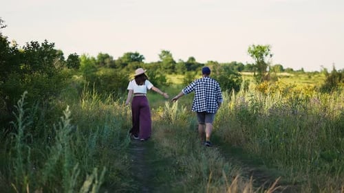 Man and Woman are Walking in the Field Holding Hands at Summer Day Filmed in Slow Motion
