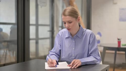 Woman Writing on Paper at Desk in Office