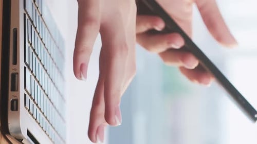 Woman Typing on Laptop, Holding Smartphone in Office