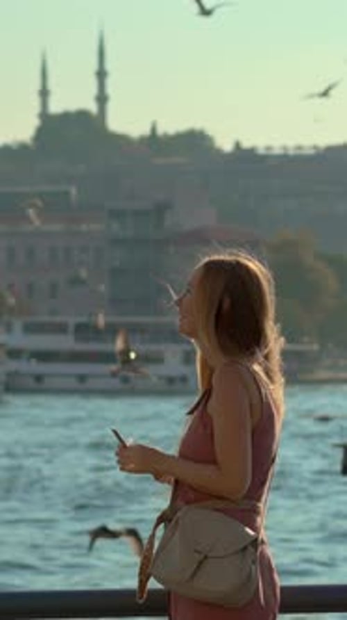 A Young Woman Stands on a Pier Engaging with Seagulls As She Playfully Attempts to Offer Them a