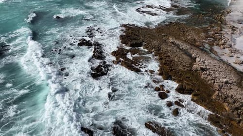 Drone flight above turquoise wave swell washing in on rugged Cape Town beach