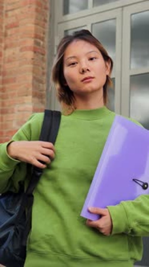 Niña segura de sí misma que sostiene una carpeta morada con una expresión seria en el campus de una escuela