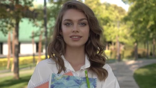 Portrait of a Young Beautiful Female Student with a Textbook in the Park Slow Motion