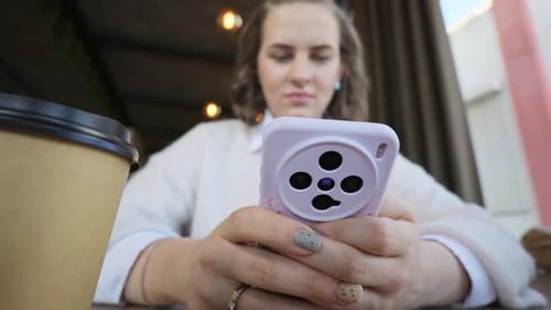 Female Hands Typing on Smartphone at Cafe Table with Coffee Cup