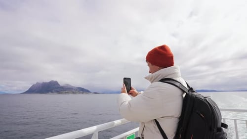 Young Man on a Ferry Taking Panorama Photo of Sea with Mobile Phone