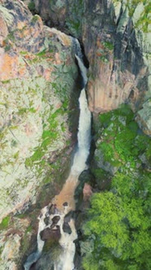 An Aerial View of a Stunning Waterfall Cascading Through Rocky Cliffs Surrounded By Vibrant Greenery