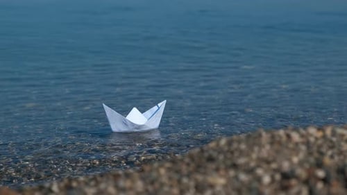 Paper Boat Floating Gently Near Pebble Beach