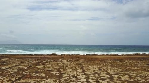 drone shot flying on desert dry landscape toward a rough sea on a cloudy and windy summer day