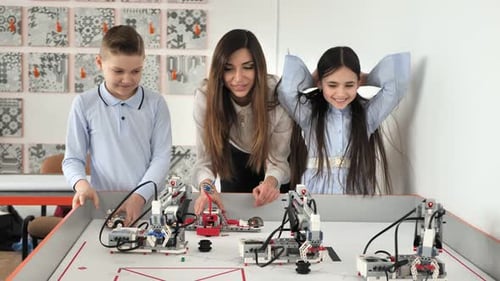 Young Beautiful Mother with Her Son and Daughter Play in the School of Robotics