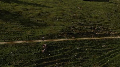 Backpacker trekking on cliffside dirt trail alone, exploring outdoors. Aerial drone shot