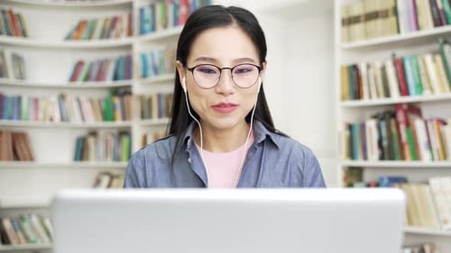 Smiling asian female student talking on video call using laptop computer sitting at university