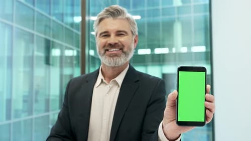Happy businessman points finger at mobile phone with green screen in business office. Color key,