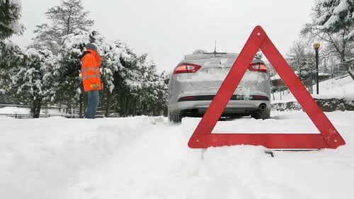 Assistance on a Snowy Road with a Brokendown Vehicle and Warning Triangle