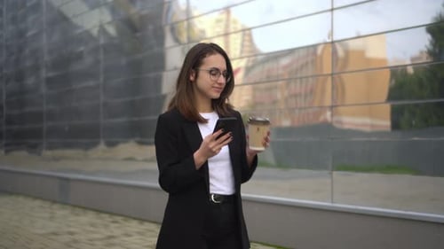 A Businesswoman Walks Down the Street Drinks Coffee and Writes on the Phone