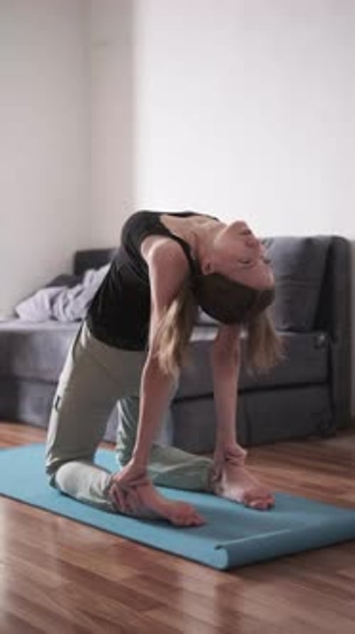 Mujer practicando yoga con la espalda doblada sobre una colchoneta en casa, estirando la flexibilidad, estilo de vida saludable