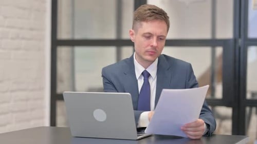 Focused Businessman Analyzing Documents and Using Laptop