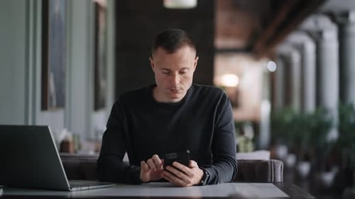 Young Adult Man Using Smartphone Sitting In Cafe With Laptop Male Person With Modern Gadgets