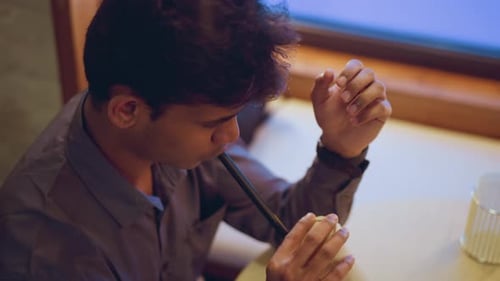 Young Man Drinking Through Straw Indoors at Table